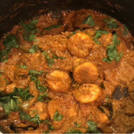 Shrimp curry with red sauce and green herbs in a black bowl