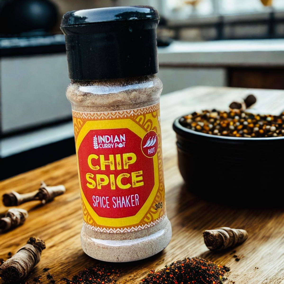 A bottle of Indian Curry Pot Spice Shaker stands on a wooden table with whole curry leaves, a small pile of ground spice, and a bowl of spices in the background.