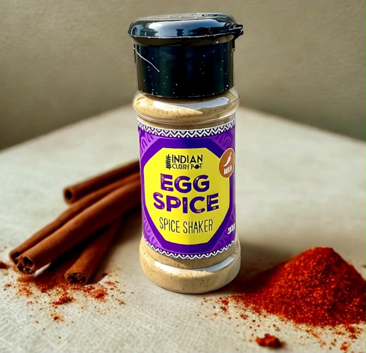 A bottle of Indian Clarity Farm Egg Spice Spice Shaker stands on a light textured surface with cinnamon sticks and red spice powder scattered around it.