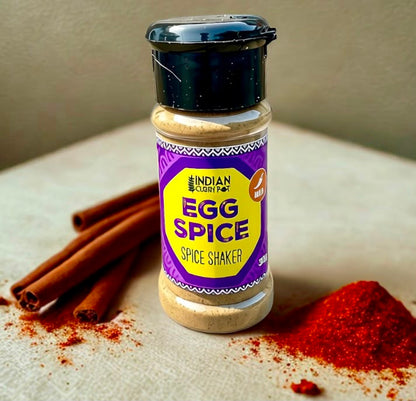 A bottle of Indian Clarity Farm Egg Spice Spice Shaker stands on a light textured surface with cinnamon sticks and red spice powder scattered around it.