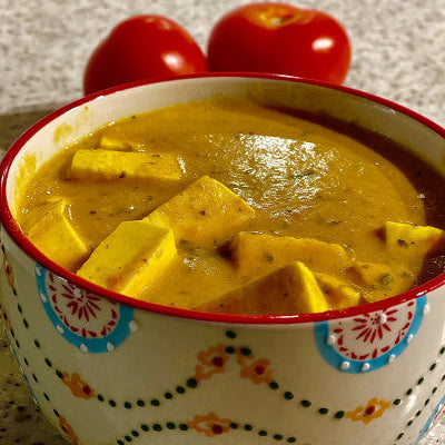 Bowl of yellow curry with tofu and tomatoes on a speckled countertop