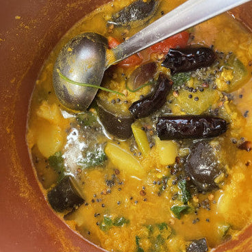 Spicy yellow curry with dark ingredients in a terracotta pot