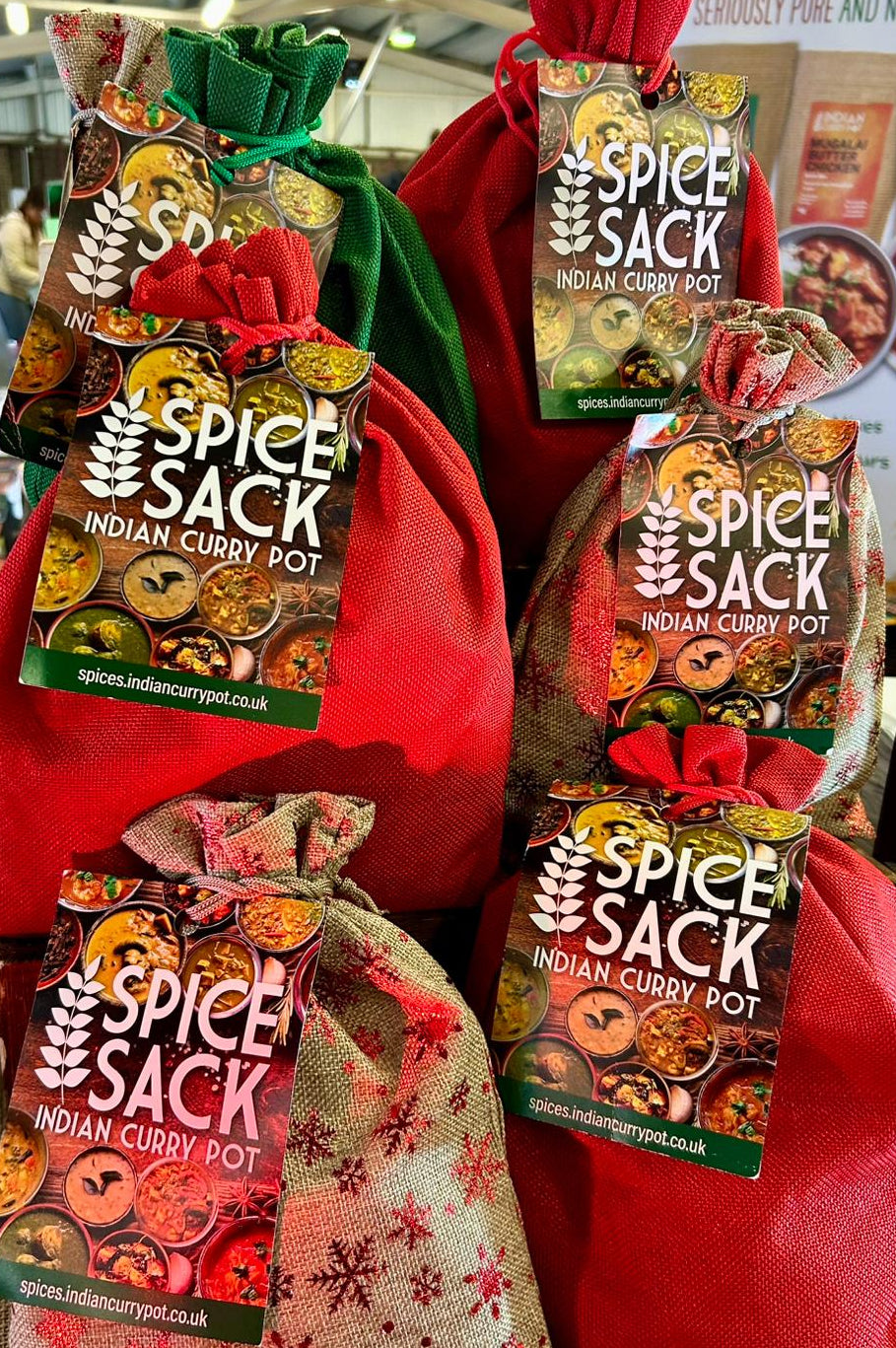 Spice Sack Indian Curry Pot packages displayed on a table with people in the background.