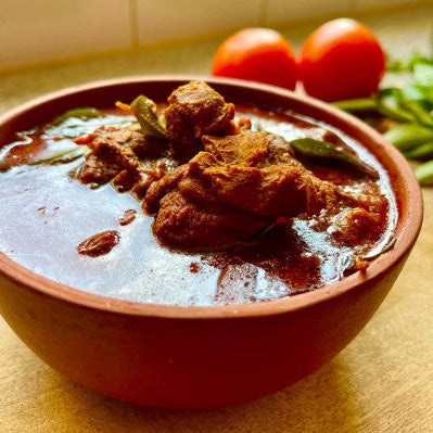 Bowl of curry with meat and vegetables on a wooden surface